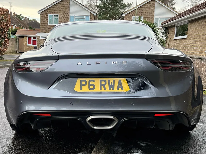 Rear view of the same grey Alpine sports car, showing slim taillights, spaced Alpine lettering, central exhaust outlet, rear diffuser and yellow UK registration plate “P6 RWA.”