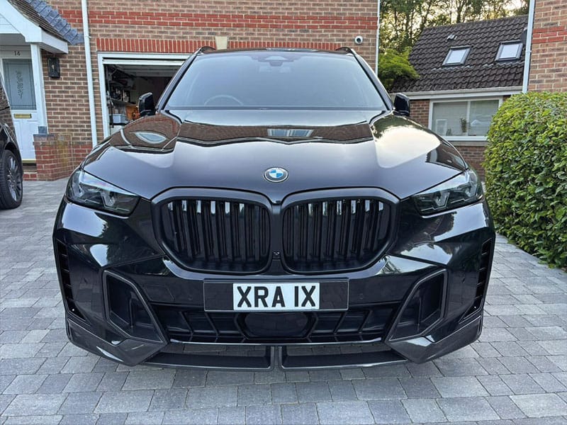 Front view of a black BMW X5, showing black kidney grilles, LED headlights and a white front number plate displaying “XRA 1X.”