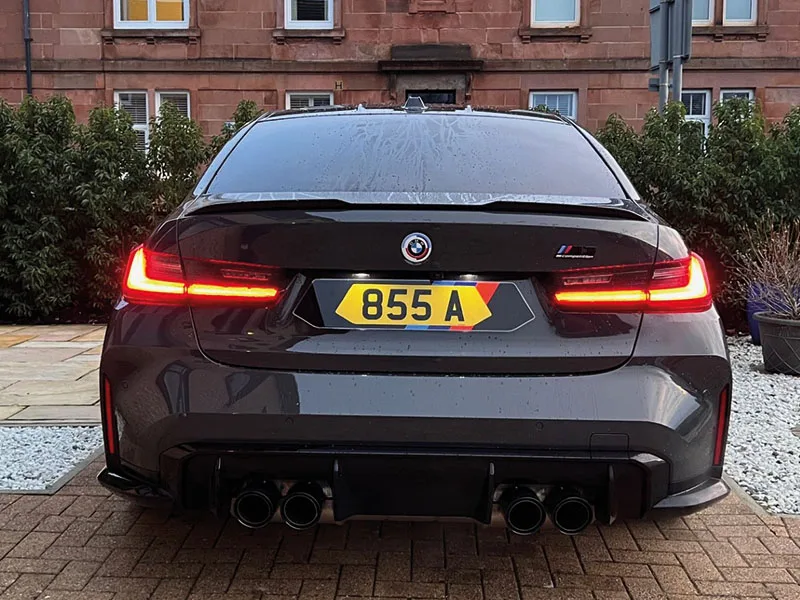Straight rear view of a grey BMW M3 G80 with illuminated LED taillights, quad exhausts and a yellow M Sport-inspired Signature number plate displaying “855 A.”