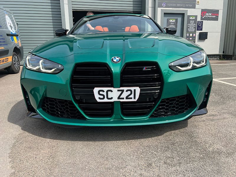 Front view of a green BMW M4 G82 Convertible with the roof down, showing the illuminated headlights, black kidney grille and white “SC Z21” number plate.