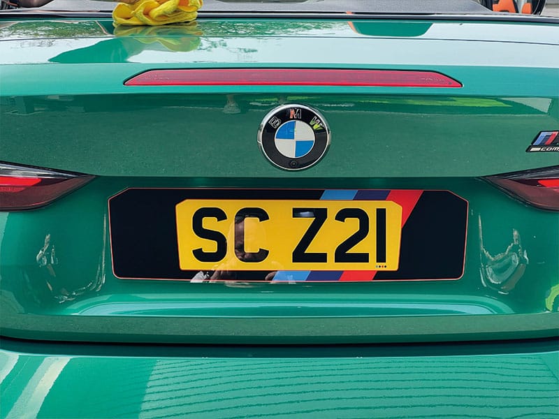 Close-up rear view of a green BMW M4 G82 Convertible, highlighting the BMW M-style colour detailing and yellow shaped number plate displaying “SC Z21.”