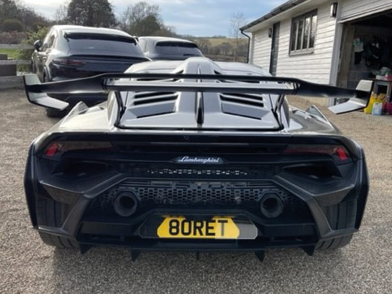 Rear view of a black Lamborghini Huracán STO, showing the large rear wing, twin central exhausts, aggressive diffuser and a yellow shaped number plate displaying “80RET.”