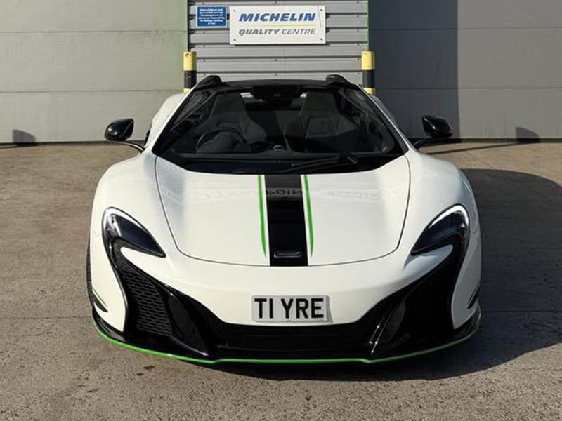 Front view of a white McLaren 650S Spider, featuring black aerodynamic detailing, green accent lines and a compact white Zero Plate displaying “T1 YRE.
