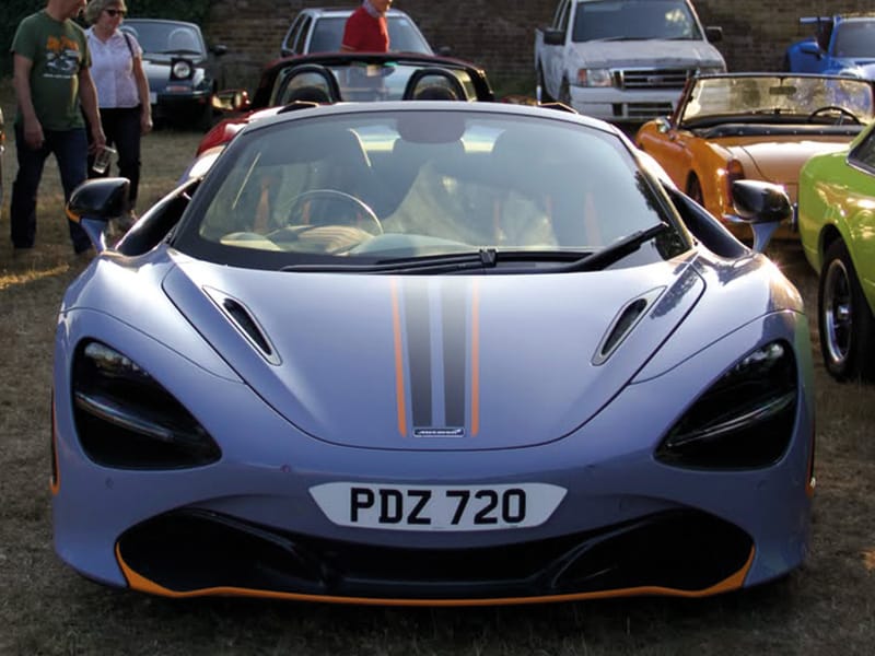 Front view of a grey McLaren 720S with orange racing stripes, featuring a white shaped number plate displaying “PDZ 720.”