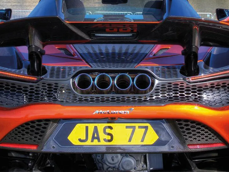 Close-up rear view of an orange McLaren 765LT Spider, highlighting the quad exhaust outlets, carbon fibre rear wing and yellow shaped number plate displaying “JAS 77.”