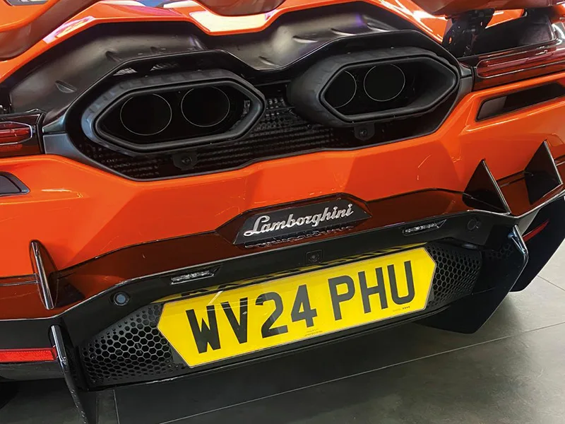 Close-up rear view of an orange Lamborghini Revuelto, featuring quad exhaust outlets and a yellow shaped number plate displaying “WV24 PHU.”