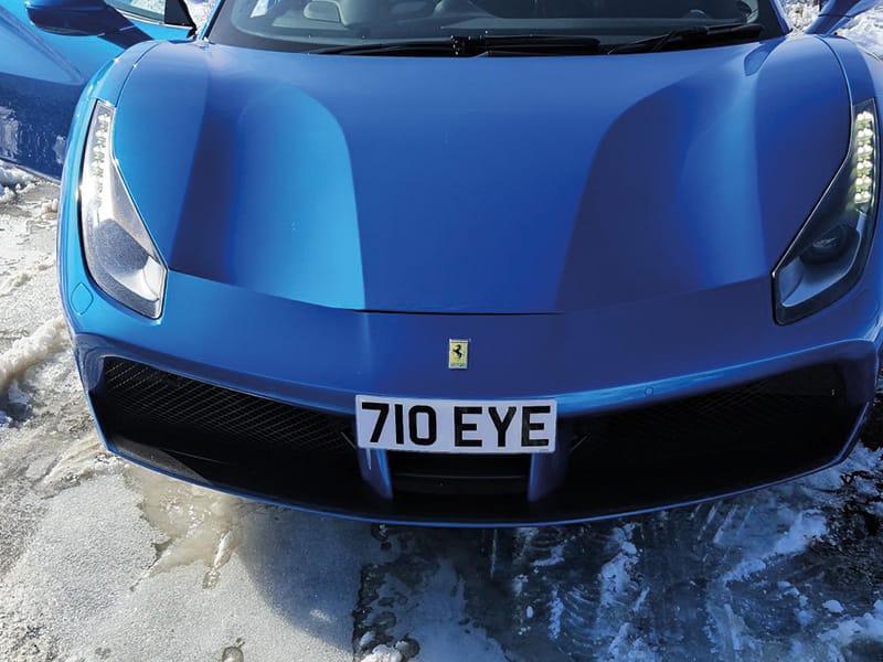 Close-up front view of a blue Ferrari 488, showing the front air intakes, Ferrari bonnet badge and compact white “710 EYE” number plate.