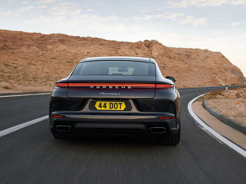 Rear view of a black Porsche Panamera fitted with a shaped yellow Signature rear number plate with black surround.