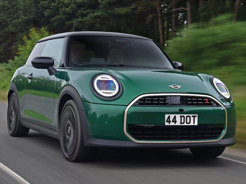 Front three-quarter view of a green MINI Cooper S driving along a road with a white 44 DOT number plate.